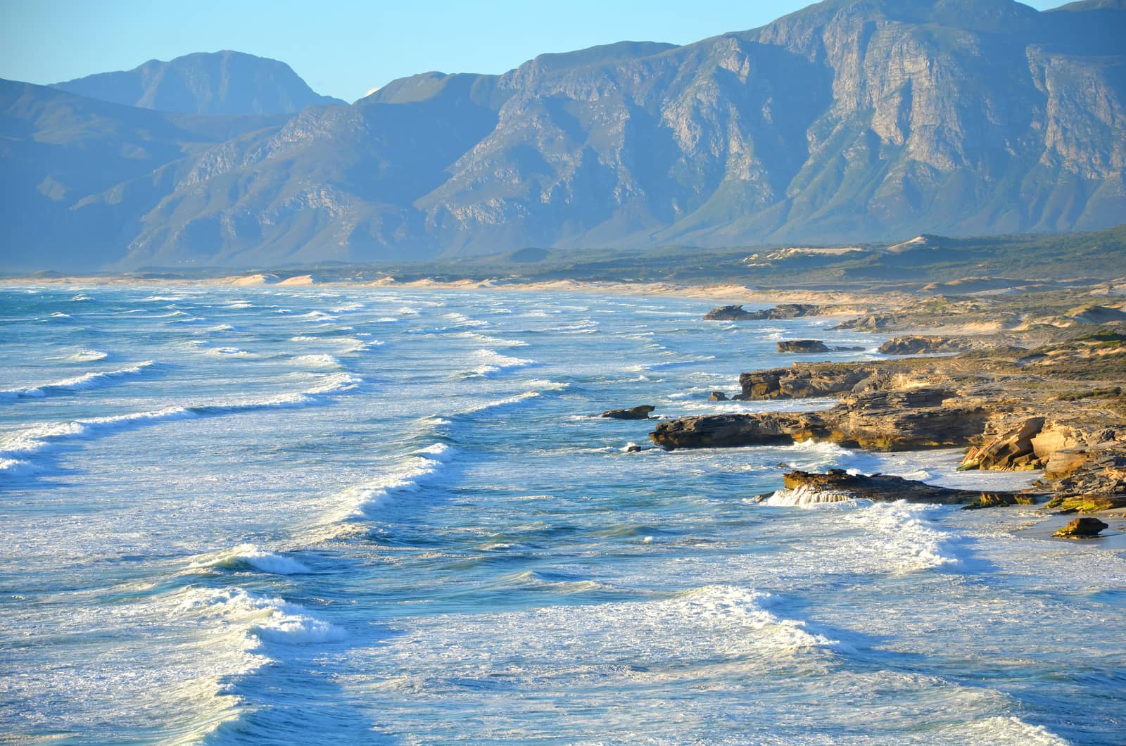 Felsküste des Western Cape mit Brandung und dahinter ansteigenden Hügeln